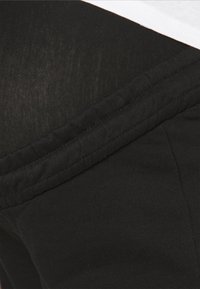 Mustapokin housut, joissa on joustava vyötärö ja sileä pinta, näyttäen läheltä kankaan ja ompelutarkkuuden yksityiskohtia.