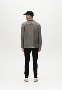Veste rayée grise avec un col en V, portée sur une chemise blanche, assortie à un pantalon noir et des baskets claires. Vue de dos affichée.