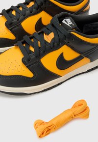 Schwarze und orange Nike-Sneaker aus Leder mit perforiertem Zehenbereich, dicken schwarzen Schnürsenkeln und zusätzlichem orangefarbener Schnürsenkel.
