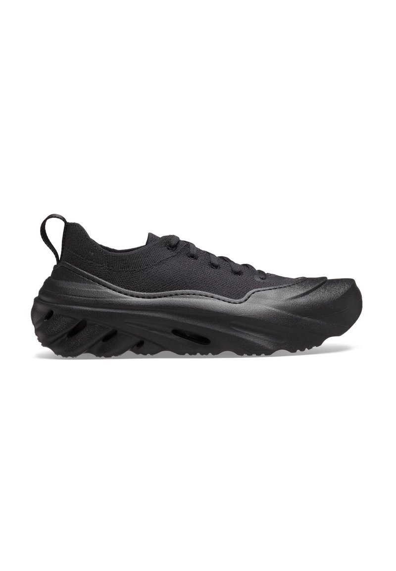 Schwarzer athletischer Sneaker mit dicker, strukturierter Sohle, gestricktem Obermaterial, Schnürdesign und Ziehschlaufe am Absatz, im Seitenprofil auf weißem Hintergrund gezeigt.
