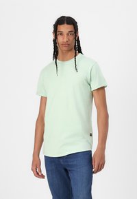 Jasnozielona koszulka z krótkim rękawem, z okrągłym dekoltem i podwiniętymi rękawami. Teksturowana tkanina, z małą metką z boku.