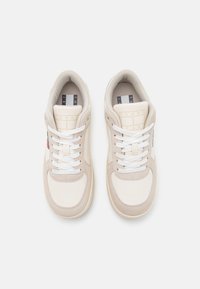 Beige och krämfärgade sneakers med vita snören, i mocka och läder, rund tådesign och logotypdetaljer på tungan och sidan.
