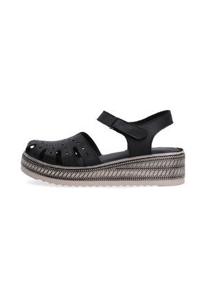 Black platform sandals with cut-out design and strap, showcasing a textured sole and decorative stitching around the base.