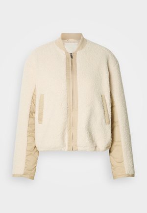 Kremo spalvos bombonešio striukė su pūkštu paviršiumi, rusvos spalvos siuvinėtomis rankovėmis, austu apykakliu ir dviem šoninėmis kišenėmis. Priekinis užtrauktukas.