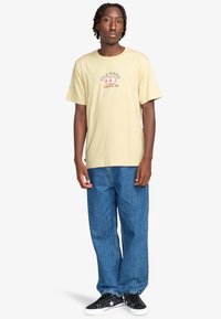 Geel katoenen t-shirt met een kleurrijk grafisch ontwerp op de voorkant. Gecombineerd met losse blauwe denim jeans en zwarte sneakers.
