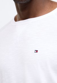 Λευκό μπλουζάκι με στρογγυλή λαιμόκοψη και κοντά μανίκια. �Διαθέτει μικρό κεντητό λογότυπο σε κόκκινο, λευκό και μπλε στο στήθος. Λείο υφή.