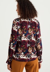 Blus med blommönster i burgundy, med långa ärmar, elastiska ärmslut och en lös passform med kontrasterande färger i brunt, gräddvitt och blått.