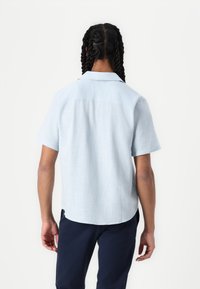 Chemise à col bleu clair à manches courtes en tissu texturé, avec un empiècement dos droit, un ourlet arrondi et des coutures soignées.