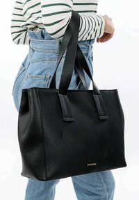 Zwart leren tote bag met gestructureerd oppervlak, twee stevige handvatten, vierkante vorm en zilveren logo detail aan de onderkant.