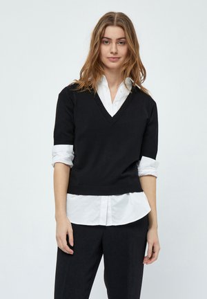 Black knitted short-sleeve sweater with a v-neck, layered over a white button-up shirt. Smooth texture, casual fit, and simple design.