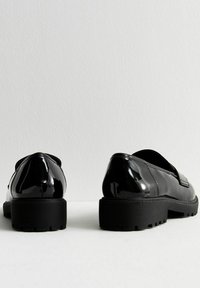 Chaussures noires en cuir verni avec une surface lisse, une forme arrondie et des semelles en caoutchouc épaisses, présentant un subtil détail de couture.
