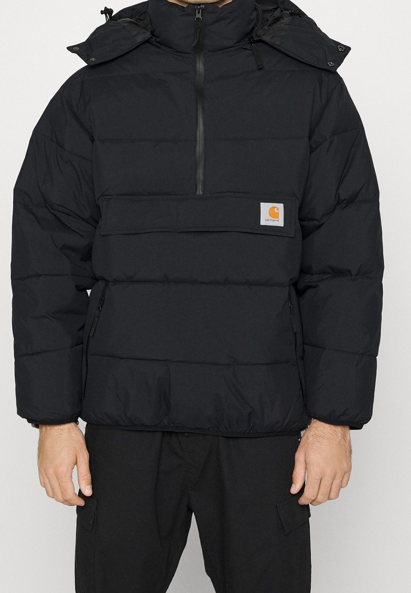 Svart puffjacka med hög krage, halvdragkedja framtill, påfällsficka och elastiska muddar. Har en logotypmärke på bröstet. Isolerad textur.