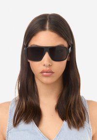 Mustad ristkülikukujulised päikeseprillid tumedate läätsedega, millel on tugev raam ja tekstureeritud aksendid külgedel.