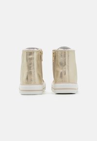 Gyllene ankelboots med en glänsande yta, sidodragkedjor och en vit sula. Den mjuka, texturerade foderöppningen längst upp ger komfort.