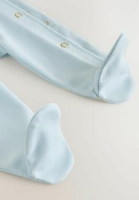 Vêtement en coton bleu clair avec une texture douce et lisse. Comprend des parties arrondies pour les pieds et des fermetures à pression à l'arrière.