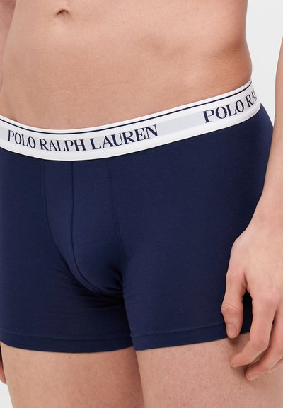 Temno modri bokserki z belim elastičnim pasom, ki nosi logo "POLO RALPH LAUREN". Gladka, raztegljiva tkanina, prilega se telesu.