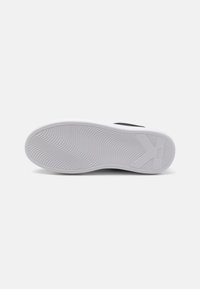 Black sneaker with a textured rubber outsole, featuring a white midsole and curved grooves for traction and grip.