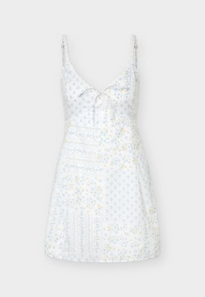 Λευκό μίνι φόρεμα χωρίς μανίκια με λεπτές ρυθμιζόμενες τιράντες, V-λαιμόκοψη, διακριτικά λουλουδάτα και γεωμετρικά σχέδια, και μια μικρή πλέξη μπροστά.