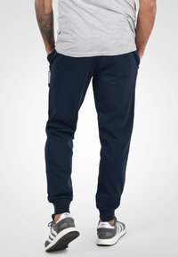 Navy blue jogger pants made from soft fabric, featuring side pockets, elastic cuffs, and a comfortable fit, paired with gray sneakers.