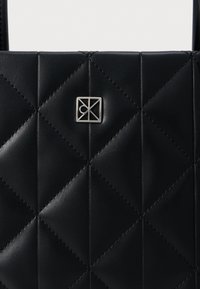 Čierna prešívaná kožená taška s vodorovným strieborným logom. Dizajn obsahuje diamantové prešitia pre väčšiu textúru a detail.