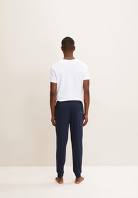 T-shirt blanc à manches courtes et pantalon bleu marine décontracté, avec une poche arrière et des chevilles retroussées, vu de l'arrière.