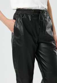 Zwarte joggerbroek van imitatieleer met een elastische tailleband, verstelbare trekkoord en zijzakken. Soepele textuur en taps toelopende pasvorm.