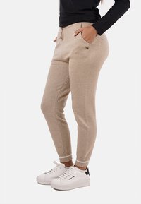 Pantaloni jogger beige con vita regolabile, tasche laterali e polsini a coste, realizzati in un tessuto morbido con una leggera lucentezza.