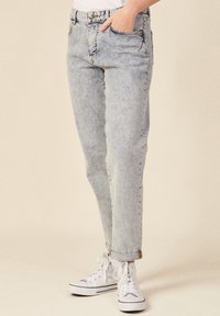 Jeans de mezclilla azul claro con corte recto, cinco bolsillos y costuras visibles. Combinados con zapatillas deportivas blancas de caña alta.