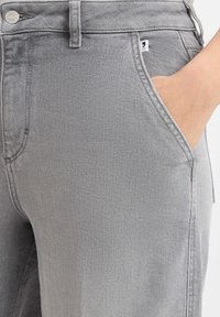 Gray denim pants featuring a front pocket, metallic button, and straight fit with subtle texture. Tag visible on the waistband.