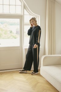 Čern�á bavlněná mikina s béžovými pruhy na ramenou, v kombinaci s černými kalhotami s širokými nohavicemi. Model má na sobě hnědé a béžové sportovní boty.