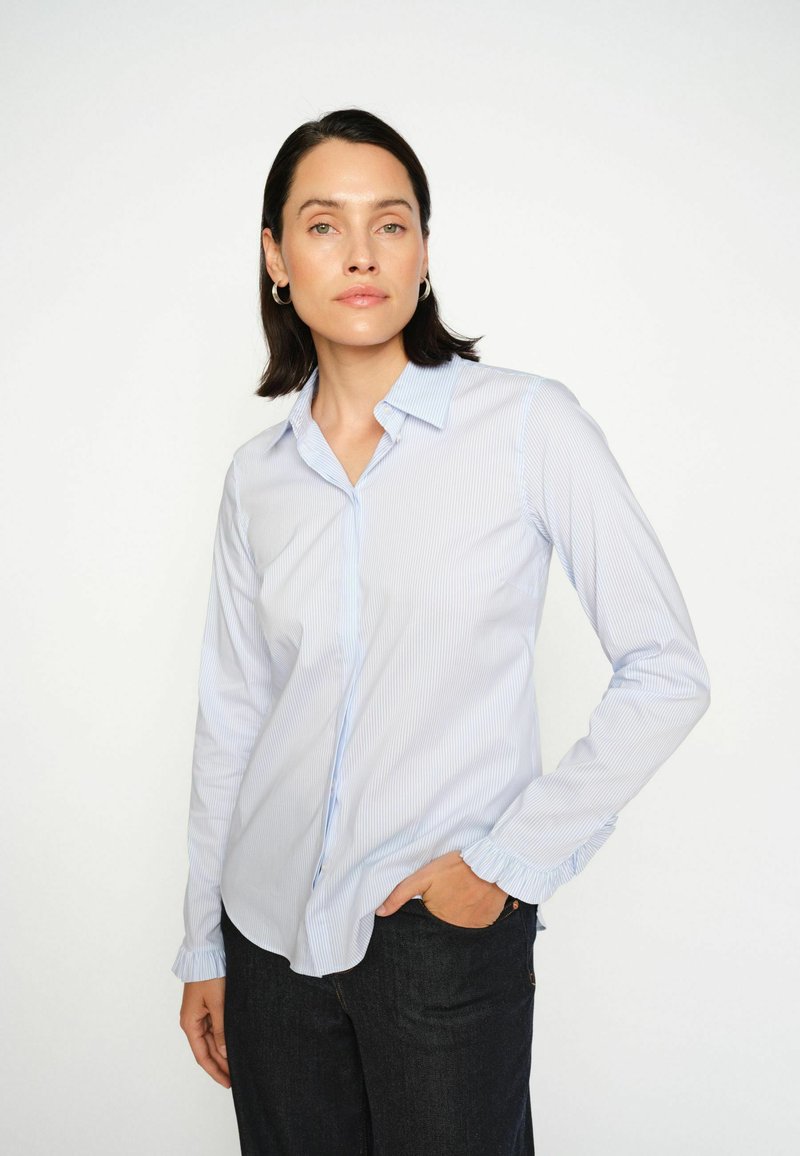 Világoskék csíkos, gallérral ellátott ing, fodros mandzsettával és sima szövet textúrával, sötét farmernadrággal párosítva.