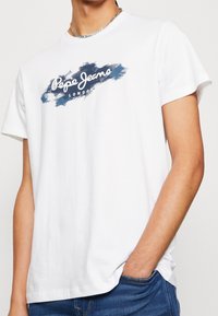 Bílá bavlněná tričko s modrým štětcovým vzorem a textem "Pepe Jeans London". Krátké rukávy a kulatý výstřih.