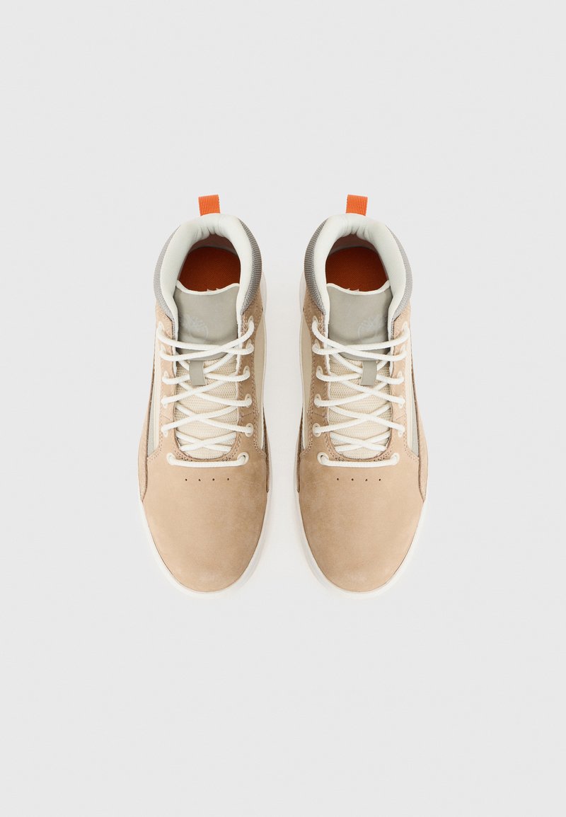 Een paar beige suède sneakers met witte veters, grijze gewatteerde kragen en oranje trekriempjes, bekeken van bovenaf op een witte achtergrond.
