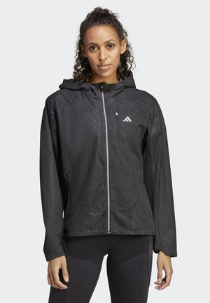 Schwarze Sportjacke mit Reißverschluss, Kapuze, strukturiertem Stoff und reflektierenden Akzenten. Sie hat ein tailliertes Design und seitliche Taschen.