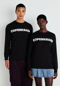Juodi ilgomis rankovėmis marškiniai su žodžiu "COPENHAGEN" ryškiu baltu šriftu, vieni derinami su purpuriniais kelnėmis, kiti - su džinsiniu sijonu.