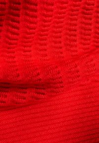 Roter gestrickter Stoff mit strukturierten Mustern und glatten Abschnitten, mit einer weichen, warmen Oberfläche und subtiler Tiefenwirkung im Design.