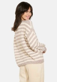 Maglione a righe crema e marrone chiaro con un taglio morbido, realizzato in tessuto morbido e testurizzato. Presenta un ampio colletto e un orlo a coste.