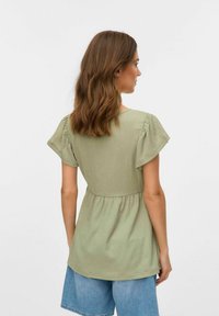 Top verde a maniche corte con tessuto testurizzato, vita arricciata e vestibilità rilassata, abbinato a pantaloni corti in denim.