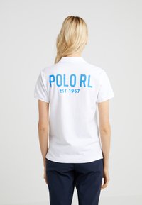 Vit polo skjorta med en blå "POLO RL" grafisk tryck och texten "EST 1967" på baksidan. Kortärmad och med en klassisk krage.