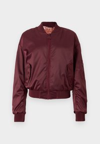 Giacca bomber bordeaux in satin liscio con polsini e orlo a costine, dotata di zip frontale e tasca laterale con dettaglio zip.