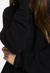 Maglione nero a coste con polsini arrotolati. Presenta un motivo testurizzato e una vestibilità morbida. Design elegante incentrato sul comfort e sul calore.