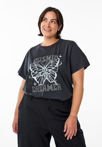 Černé oversize tričko s grafickým motivem motýla a textem "COSMIC DREAMER" posetým kamínky. Krátké rukávy s volným střihem, vyrobeno z měkké bavlny.