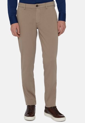 Pantalon beige avec une coupe droite, fabriqué à partir d'un tissu lisse, comportant une poche avant, une fermeture à bouton et des passants de ceinture, porté avec des baskets noires.