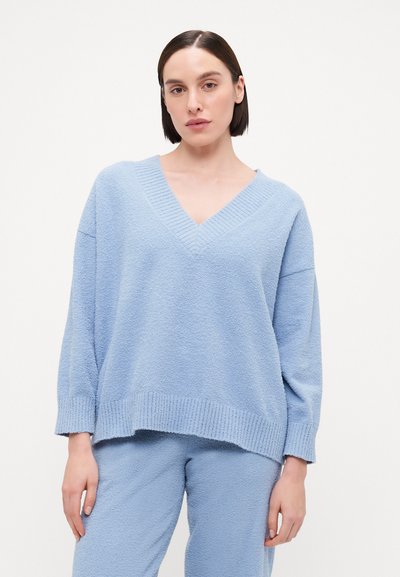 Pull en maille texturée bleu clair avec un col en V, coupe ample et poignets côtelés, associé à un pantalon assorti dans le même tissu et la même couleur.