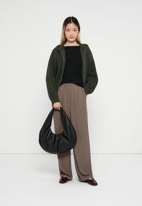 Maglione a zip a coste verde oliva, top nero aderente, pantaloni beige a gamba larga, con una borsa hobo nera e scarpe slip-on bordeaux.