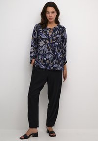 Blusa blu navy con motivo paisley, scollatura rotonda e dettaglio con fiocco. Abbinata a pantaloni neri larghi e sandali neri con tacco.