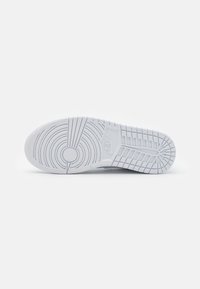 Semelle blanche de chaussure Nike avec des motifs de bande de roulement circulaires et en grille, présentée sur un fond clair uni.