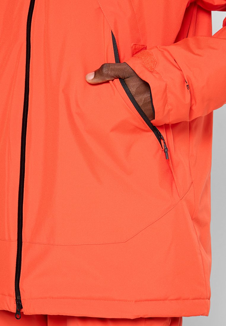 Orange wasserdichte Jacke mit einer seitlichen Reißverschlusstasche, ausgestattet mit schwarzen Reißverschlüssen und Nähten. Glatte Textur und ergonomisches Design.
