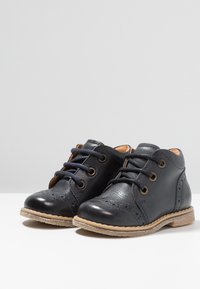 Stivali alla caviglia in pelle nera con una finitura liscia, punta rotonda, design con lacci e perforazioni decorative nella zona delle punte. Suola beige.