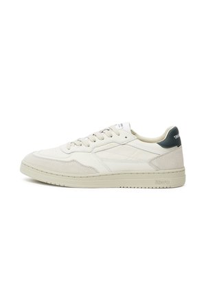 Beige leather sneakers with suede accents, flat laces, a prominent rubber sole, and a dark green heel detail; minimalist design.